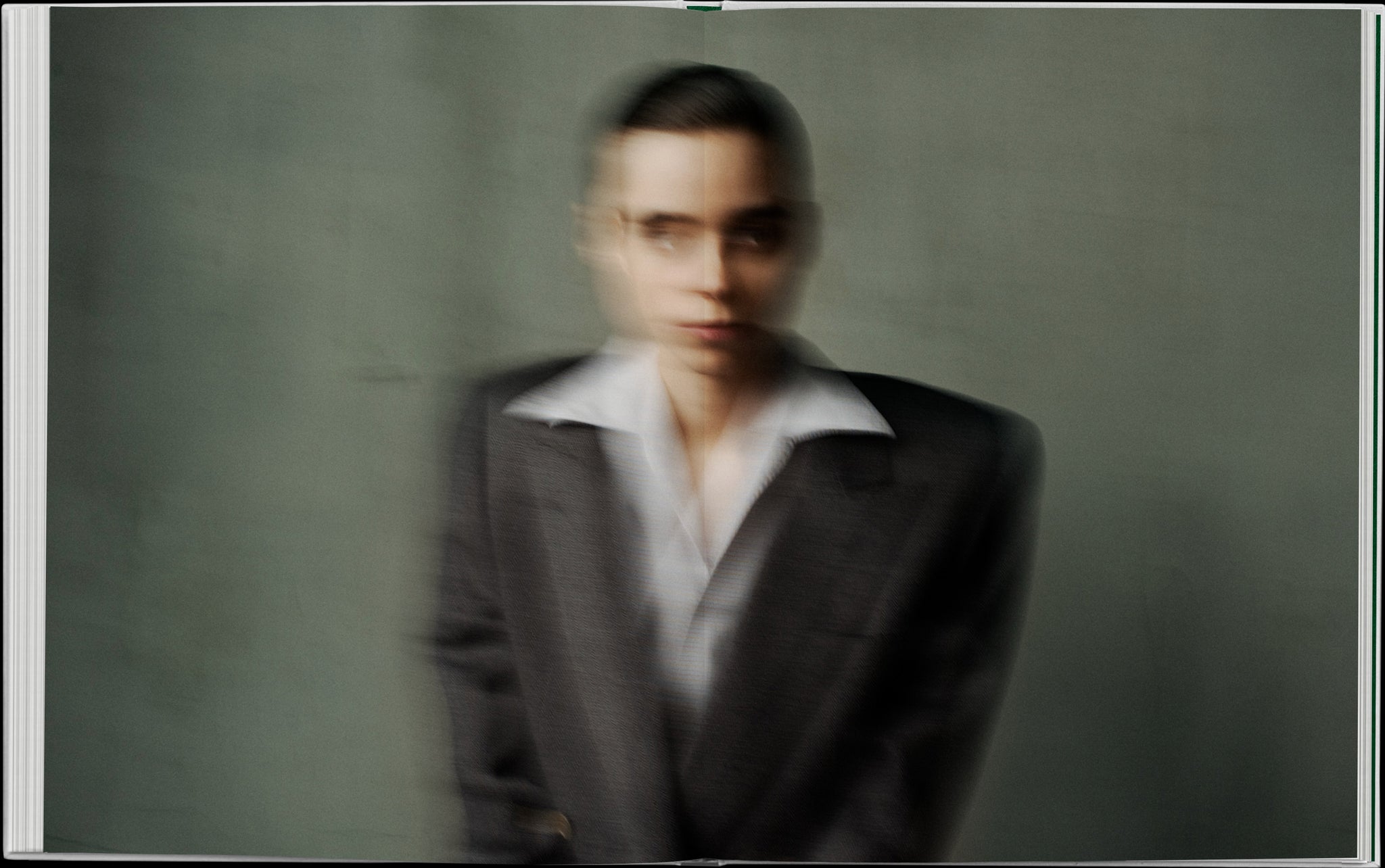 Book layout. Double spread. Blurred image of a girl in a suit with a white collar out. Greenish-grey background.