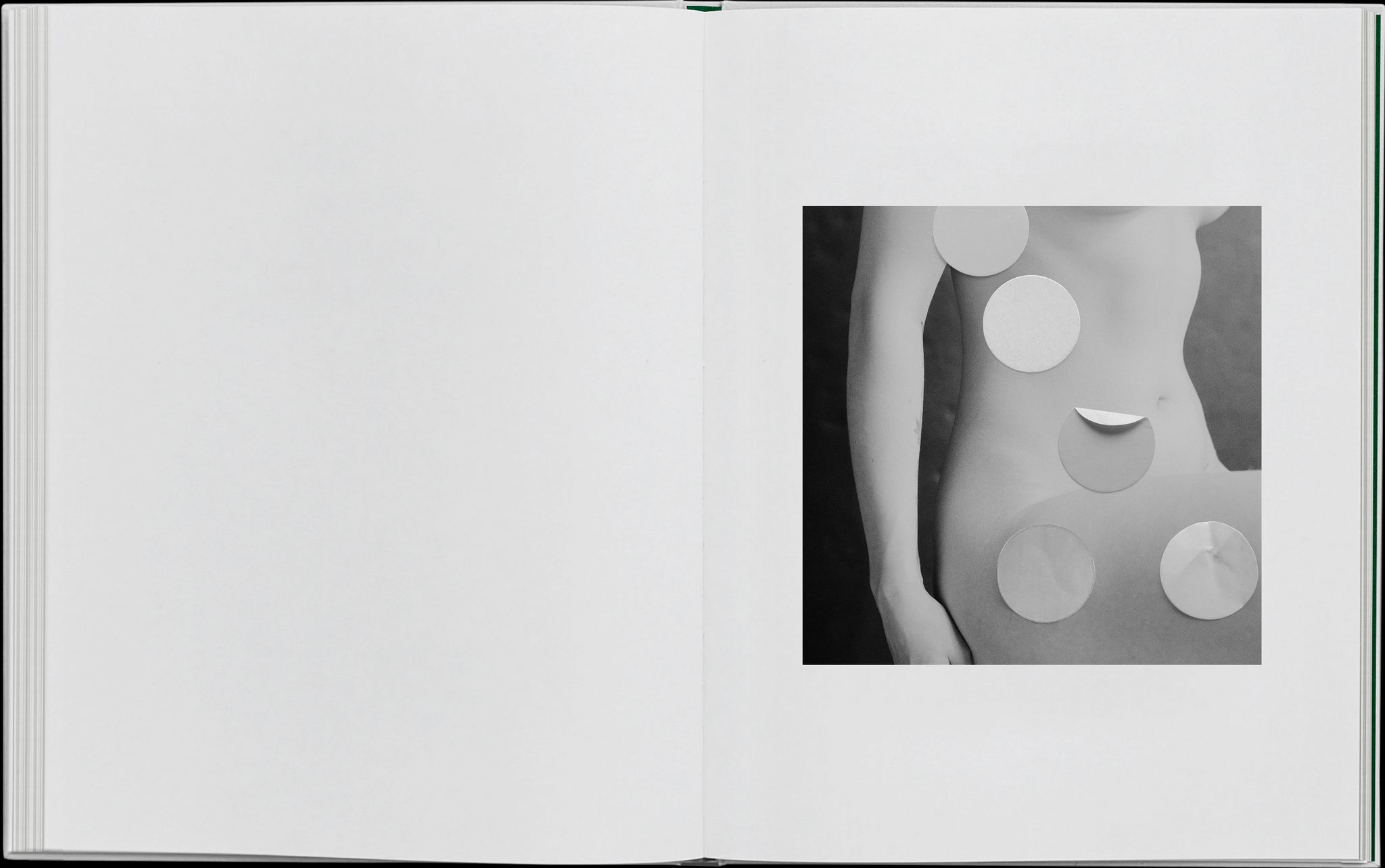 Book layout. Right: Black and white image of a nude belly and thigh. Collage element of round stickies placed upon the body.